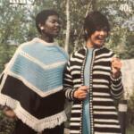 Two women wearing stylish crocheted outerwear pose outdoors in a natural setting.
