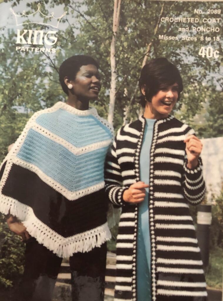 Two women wearing stylish crocheted outerwear pose outdoors in a natural setting.