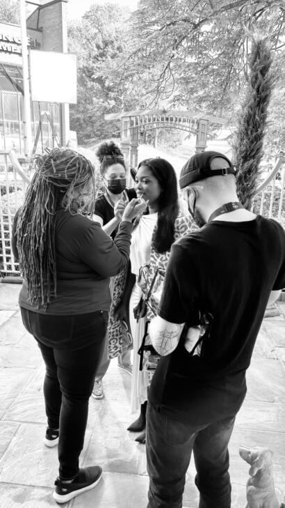 Model getting makeup touch-up outdoors, surrounded by team members.