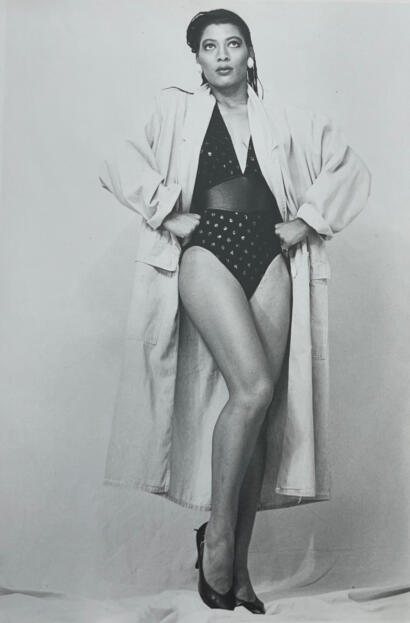 Woman in polka dot lingerie with a trench coat over her shoulders, standing confidently.
