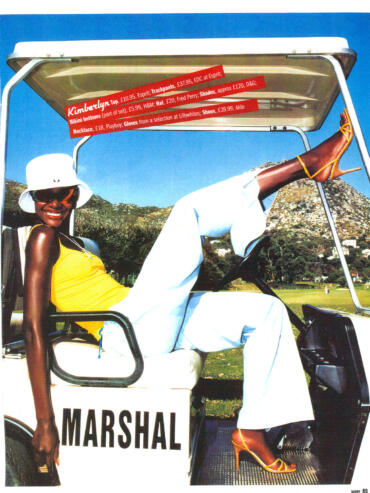 Stylish woman in yellow top and white pants, sitting on a golf cart with mountain backdrop.
