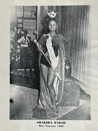 Black-and-white photo of Shakira Baksi, Miss Guyana 1967, wearing a sash and evening gown with a confident smile.