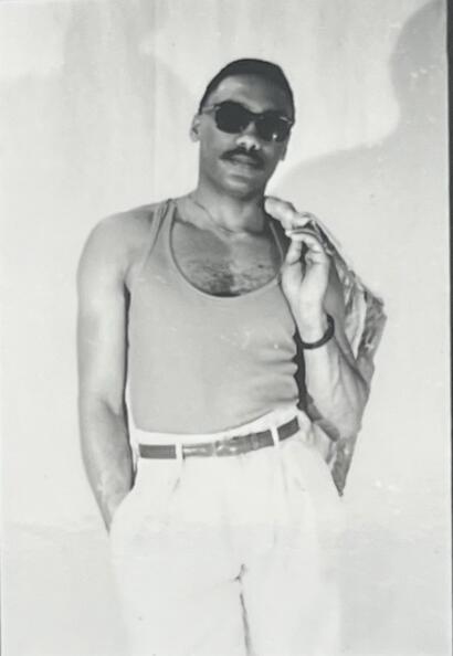Man in vintage tank top, sunglasses, and carrying a bag over shoulder, stylish and confident.