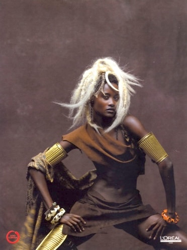 Model with platinum dreadlocks and bold accessories, photographed in earthy tones.