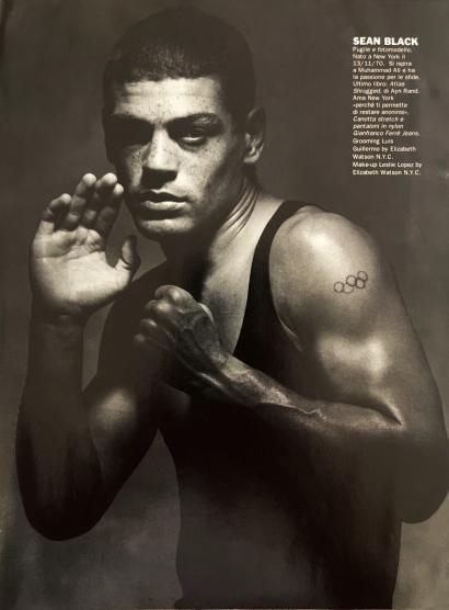 Black and white portrait of Sean Black, a young athlete with a tattoo of Olympic rings on his arm, in a boxing stance.