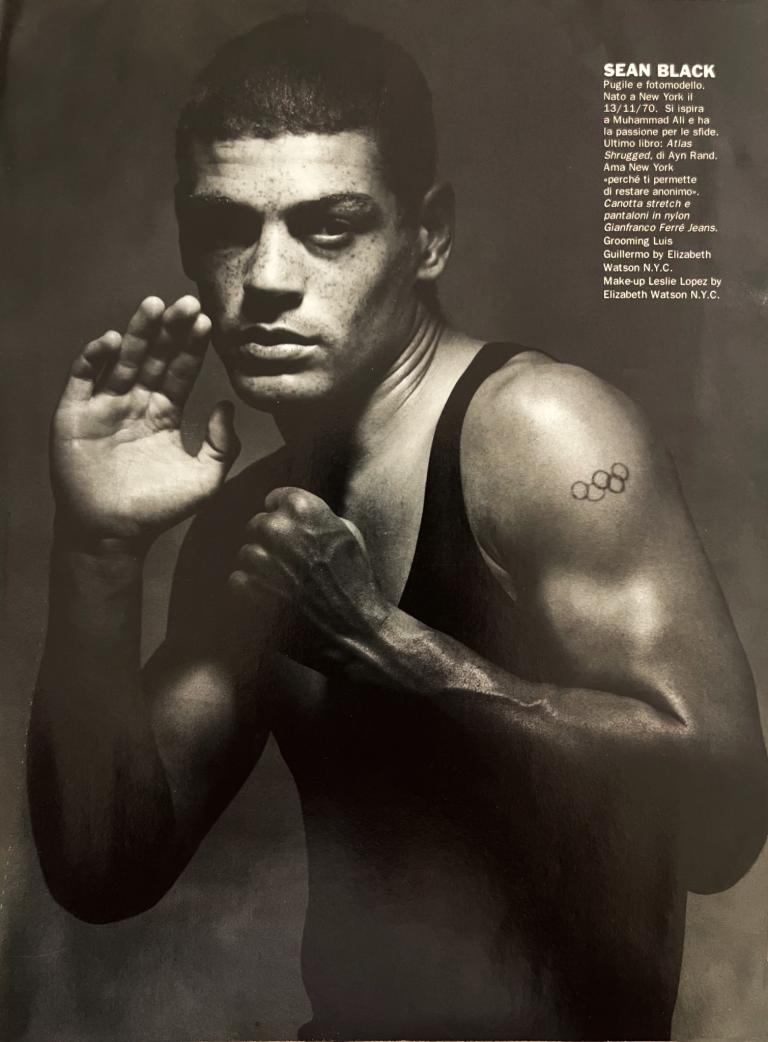 Black and white portrait of Sean Black, a young athlete with a tattoo of Olympic rings on his arm, in a boxing stance.