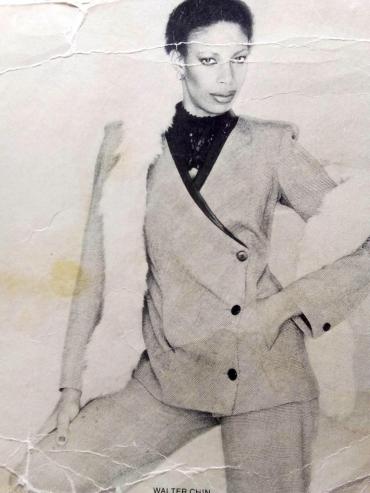 Black-and-white photo of a stylish woman in a tailored blazer, black lace top, and high-waisted pants, striking a confident pose.