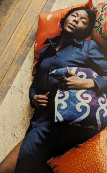 Woman lying on colorful pillows on a wooden floor, dressed in a denim shirt.