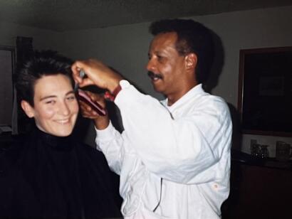 A hairdresser styles a woman's hair in a casual setting.