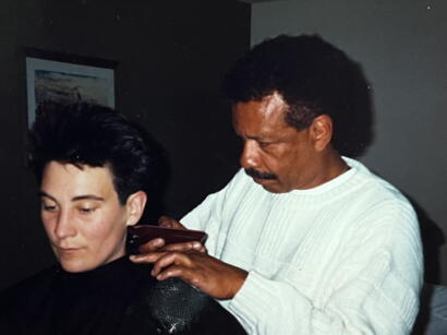 Man giving a hairstylist a haircut, with a focused expression, in an indoor setting.