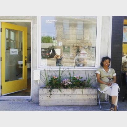 Woman sitting outside a boutique with a yellow door, smiling in casual fashion.